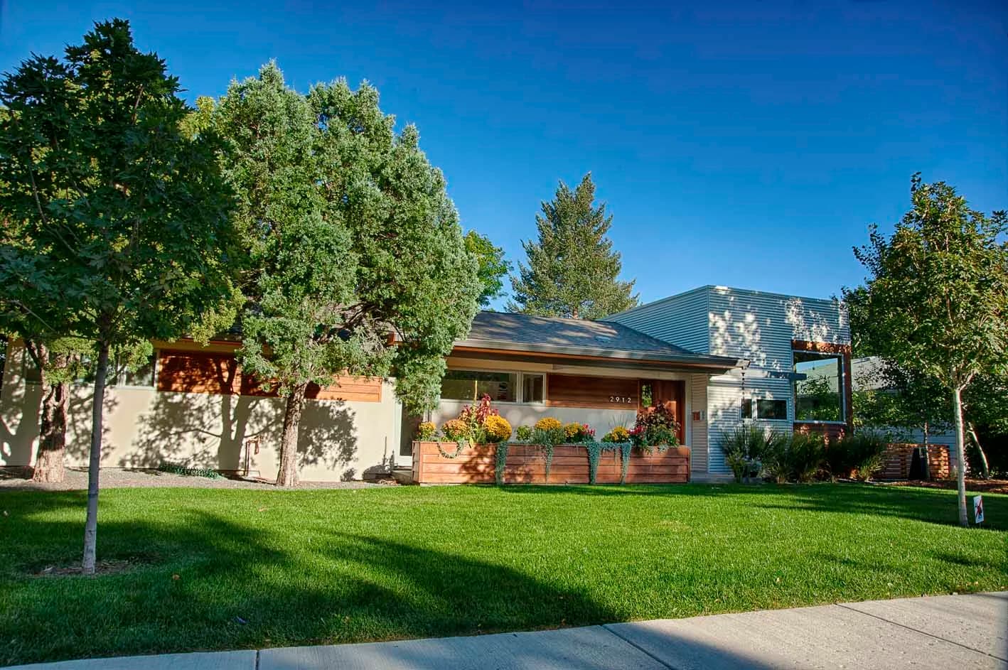 Front of a modern Sightline home with stucco, cedar and corrugated metal walls behind a cedar planter full of flowers