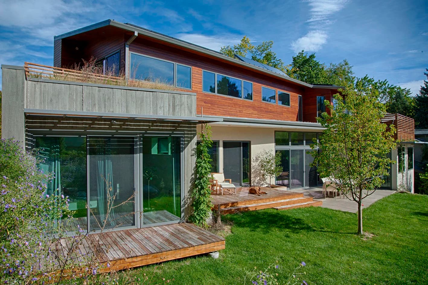 Rear of a two-storey Sightline home in cedar, board-formed concrete and glass, with decks over a green lawn